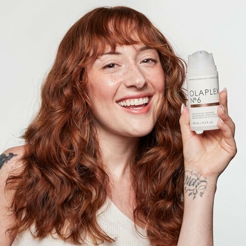 Smiling woman with red hair holding Olaplex No. 6 product.