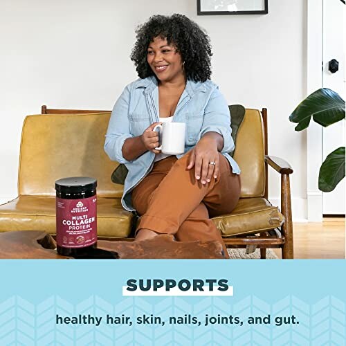 Woman sitting on a couch holding a mug with collagen protein container on table.